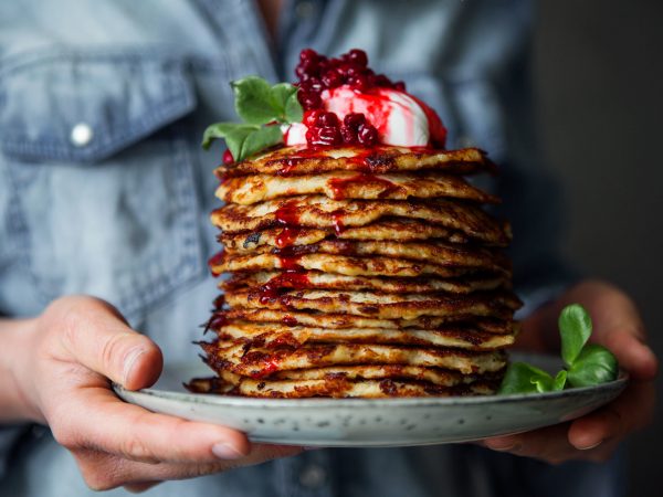 En hög med raggmunkar med klarröd lingonsylt på en tallrik. A pile of potatoes pancakes on a plate with red lingonberry jam on top.