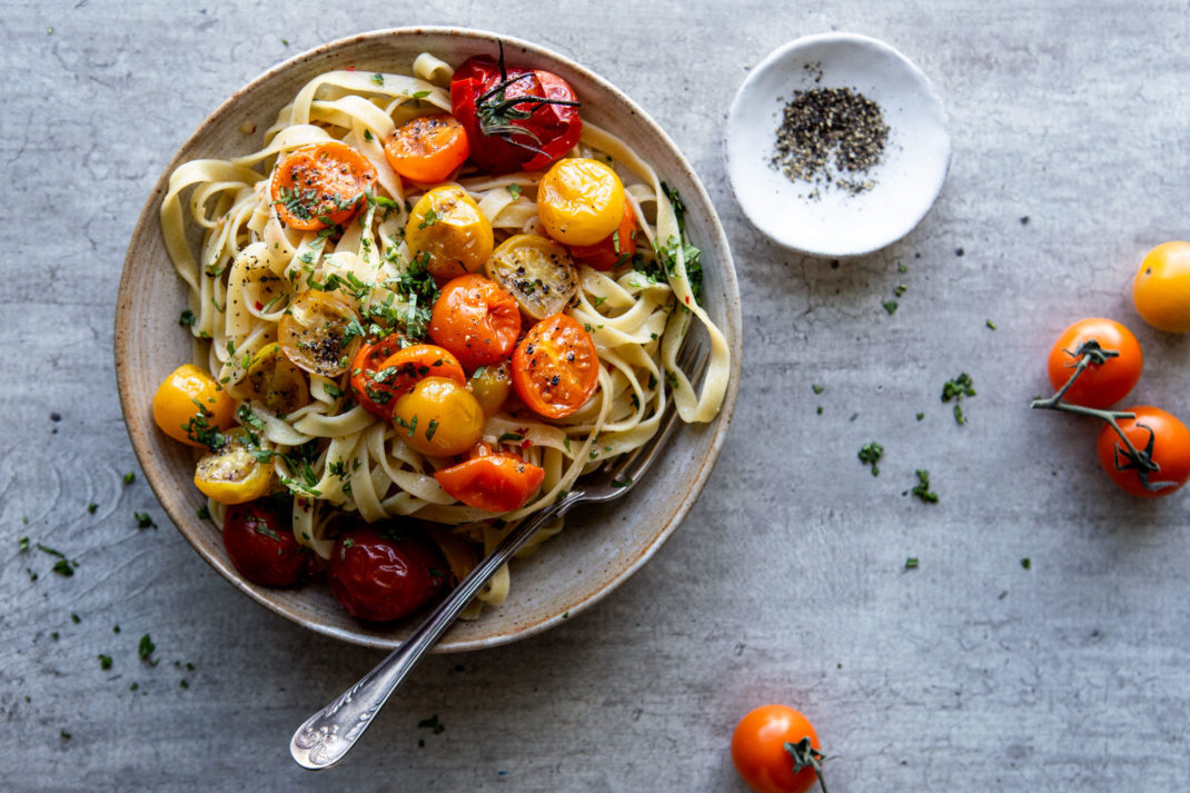 En tallrik med stekta små tomater och pasta.
