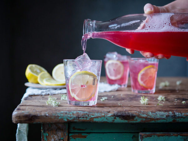 I ett mörkt rum häller någon upp en rosaröd dryck i ett glas fullt med is och citroner.