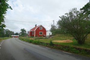 Ett rött hus ligger alldeles vid en asfaltsväg.