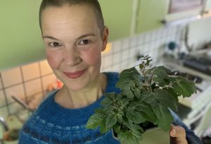 Sara står i ett kök och håller en liten tomatplanta i handen.